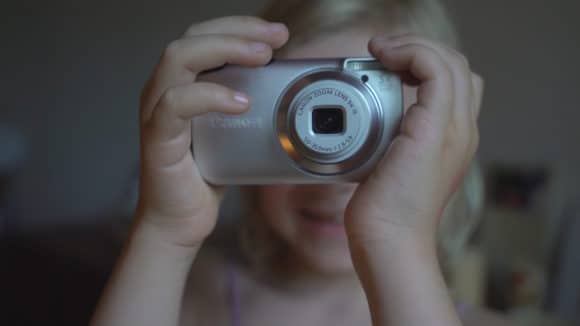 Eine blonde Frau hält eine Fotokamera vor ihr Gesicht.