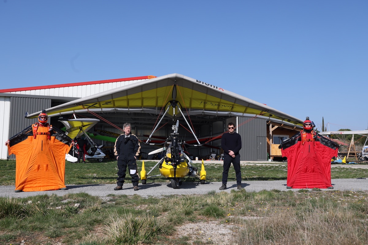 Zwei Männer mit Wingsuits stehen links und rechts neben einem Ultraleichtflugzeug 